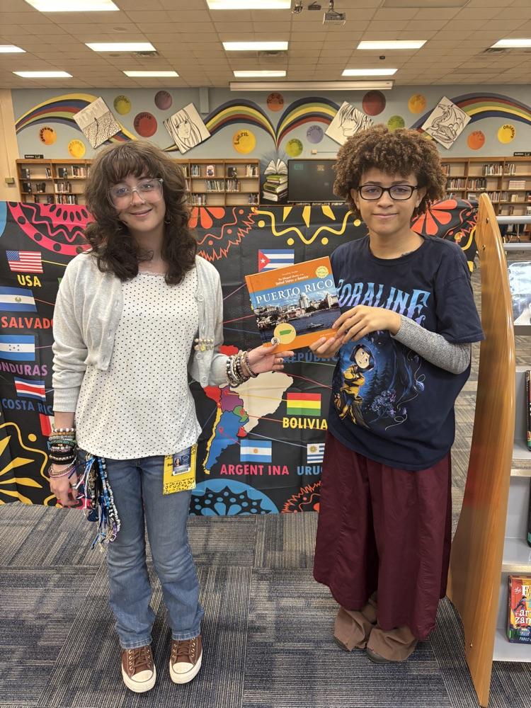 Students holding a book in front of a banner