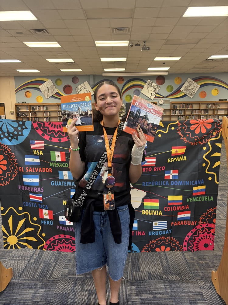 Students holding a book in front of a banner