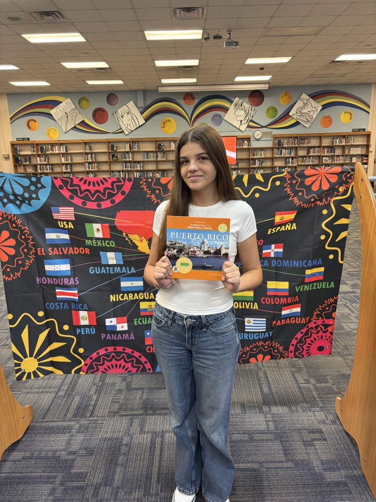 Students holding a book in front of a banner