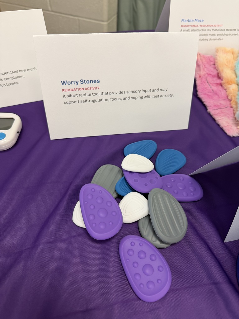 A table displays worry stones, small, textured stones, with a card describing them and a device nearby.