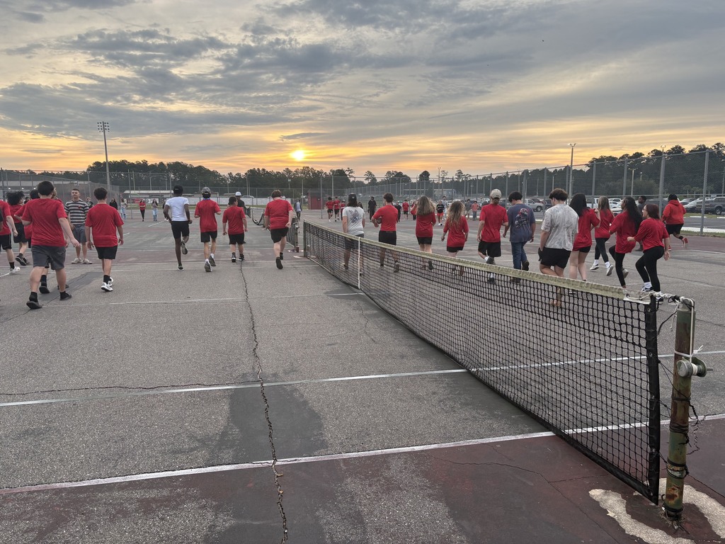 Students warming up on the tennis court jogging.