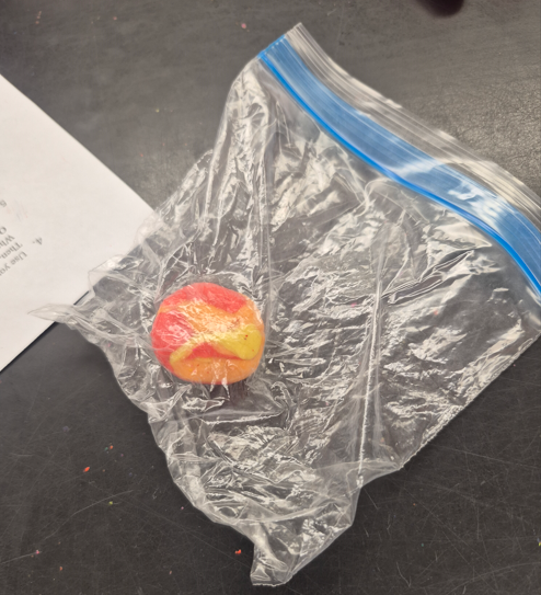 A plastic bag with blue zipper partially covering a round orange and yellow object, placed on a gray surface.