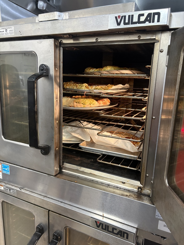 An oven with its door open and two racks of food inside. The oven is a large, stainless-steel appliance.