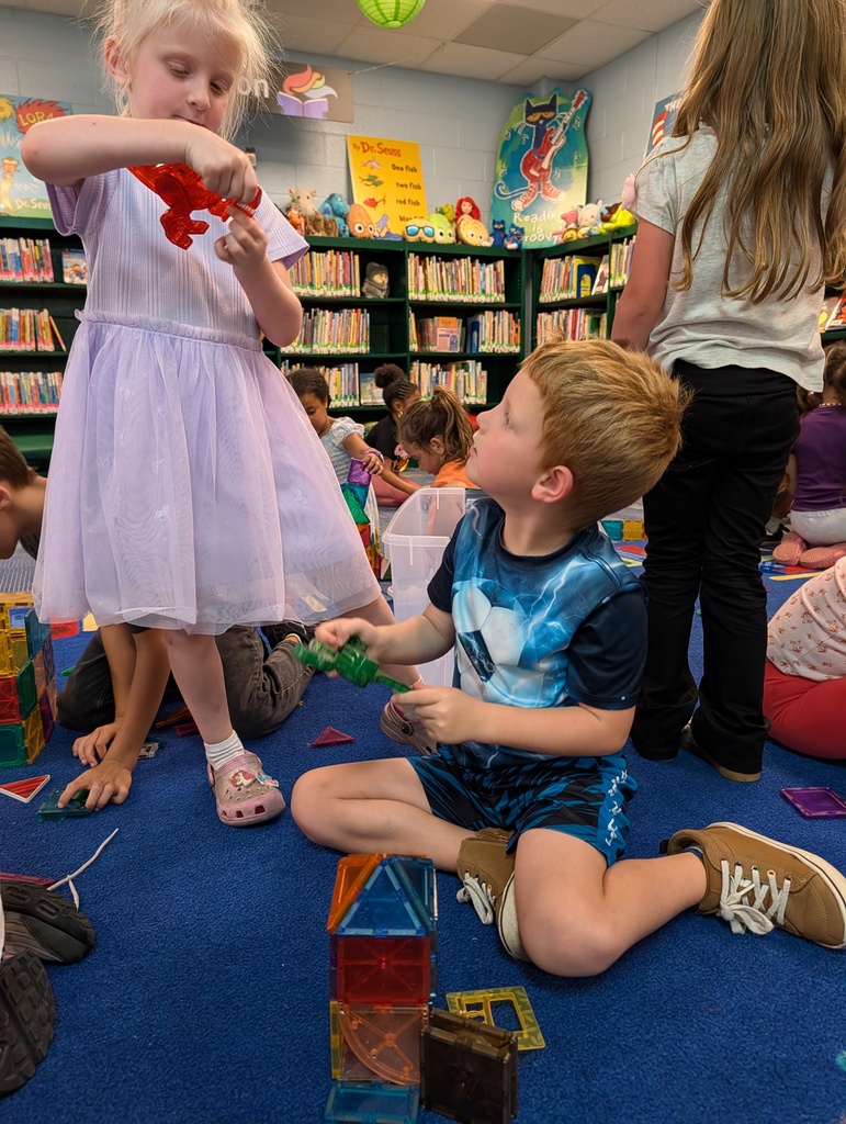Children in a library, a girl in a pink dress and a boy in a blue shirt play with blocks.