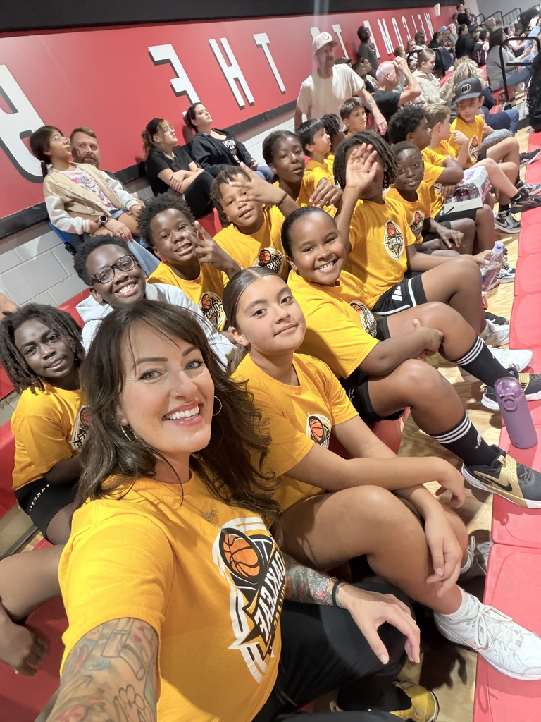 Group of youth and adults in yellow t-shirts sitting in a sports stadium. A woman smiles at the camera.