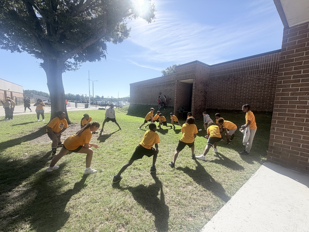 A group of young people in yellow shirts and shorts playing a game on a grassy field.