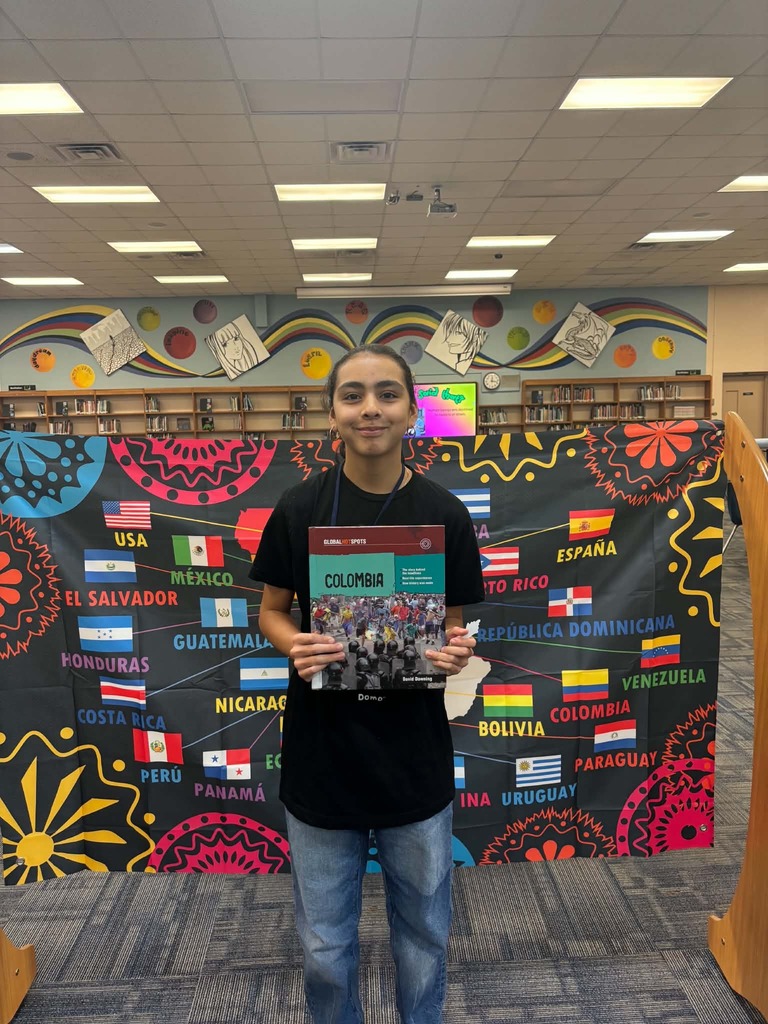 Person holds a book in front of a colorful backdrop displaying flags and country names.