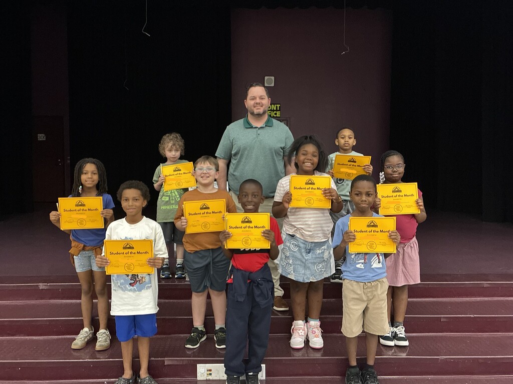 A group of students posing on stage holding "Student of the Month" certificates with Principal Martin