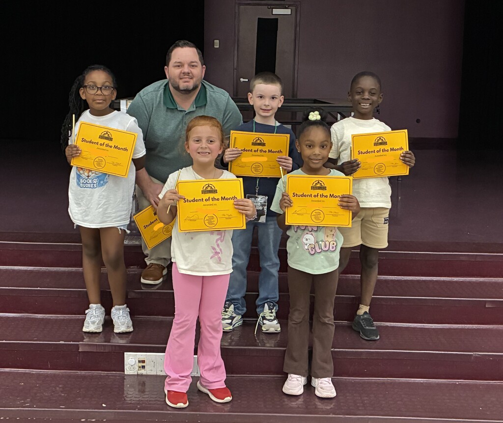 A group of students posing on stage holding "Student of the Month" certificates with Principal Martin
