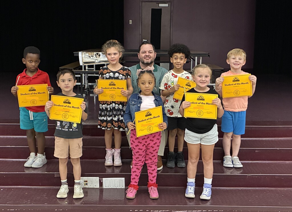 A group of students posing on stage holding "Student of the Month" certificates with Principal Martin