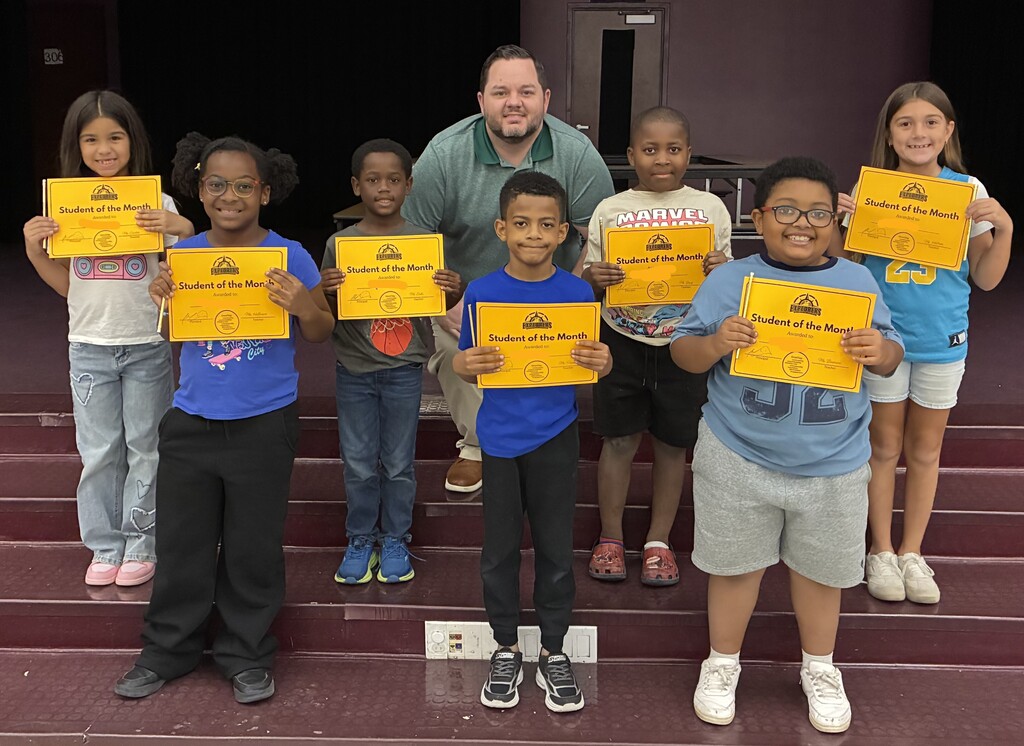 A group of students posing on stage holding "Student of the Month" certificates with Principal Martin