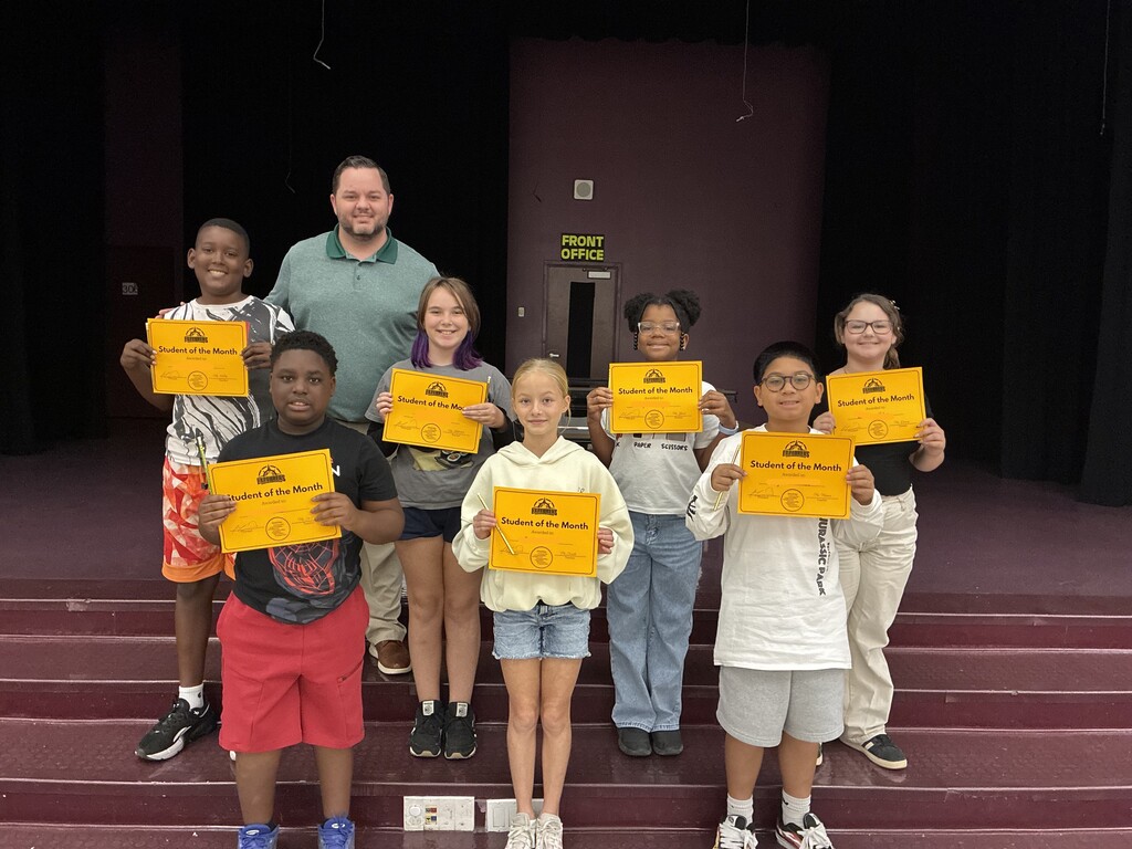 A group of students posing on stage holding "Student of the Month" certificates with Principal Martin