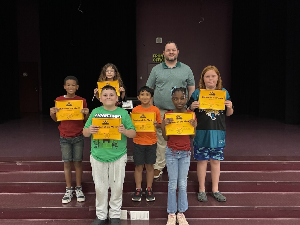 A group of students posing on stage holding "Student of the Month" certificates with Principal Martin