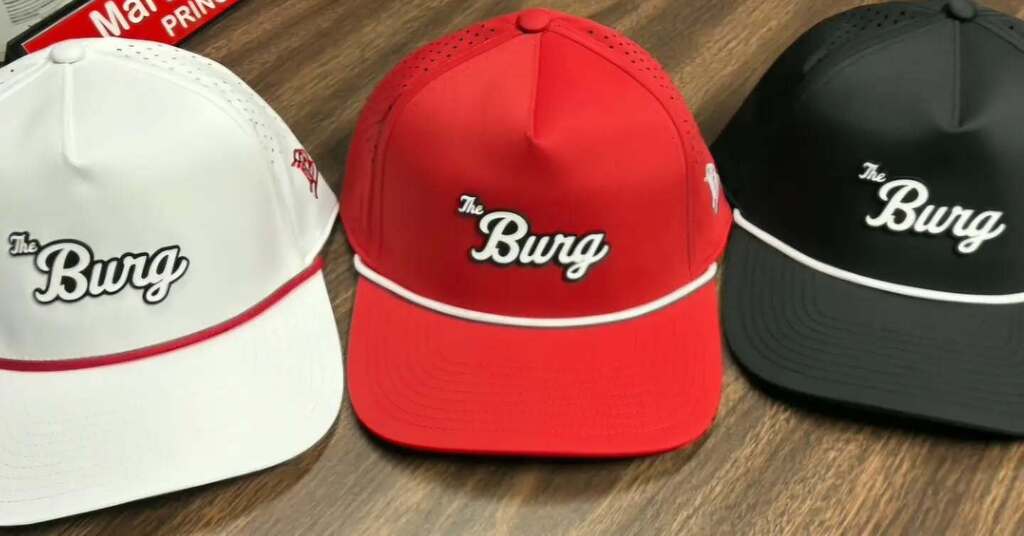 Three baseball caps with "Burg" written in white. One is white, one is red, and one is black.