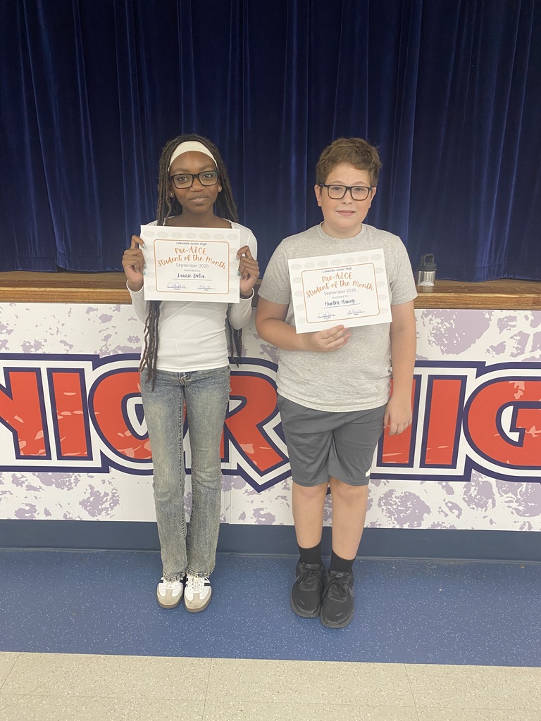 Two children stand with certificates in hand in front of a banner with red and blue letters.