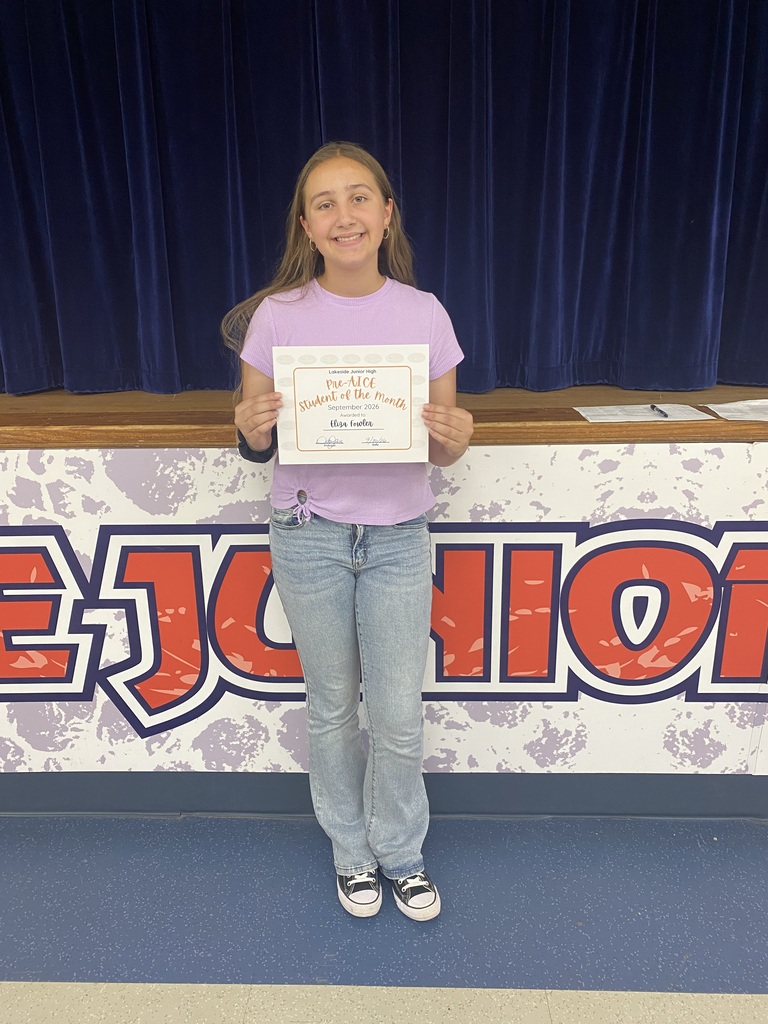 A girl holds an award in front of a stage with a banner reading "JUNIOR HIGH".