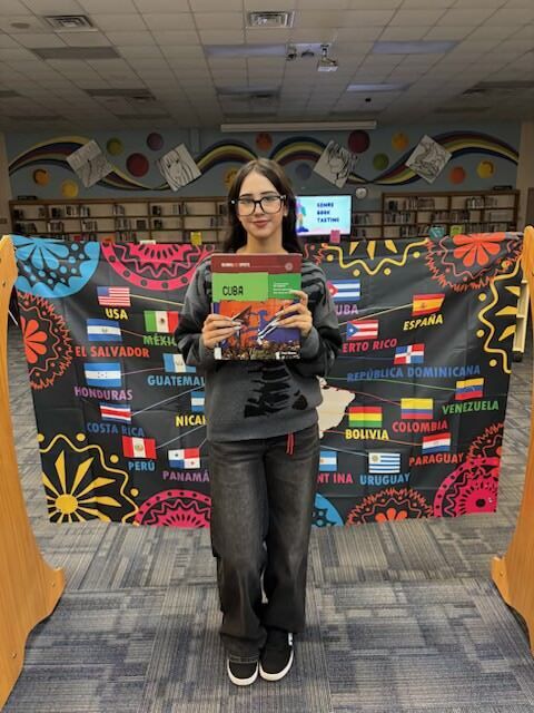 Woman in black shirt holding book, standing in front of a large display of flags.