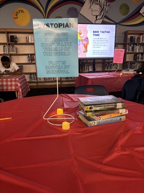 A round table with a red tablecloth. A blue sign reading "Stopian" stands above a stack of books. Two people sit at tables in the background.