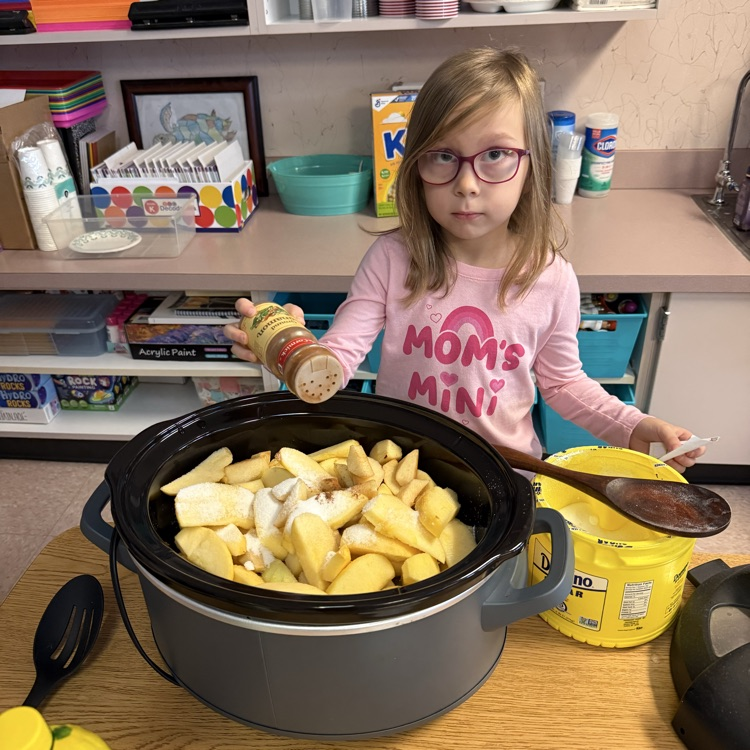 Girl shakes spice over a pot of apples.