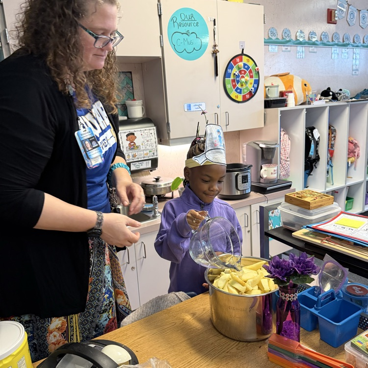 teacher and student stand with a pot of apples and pour water over them