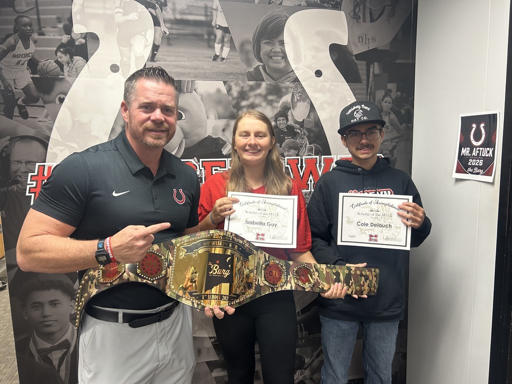 Three people stand together holding certificates and a belt, with a wall mural featuring sports figures and a logo in the background.