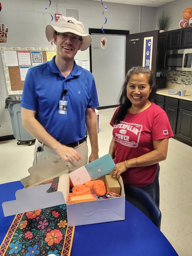 A man and a woman are standing by a table. They are both smiling and appear to be presenting a box.