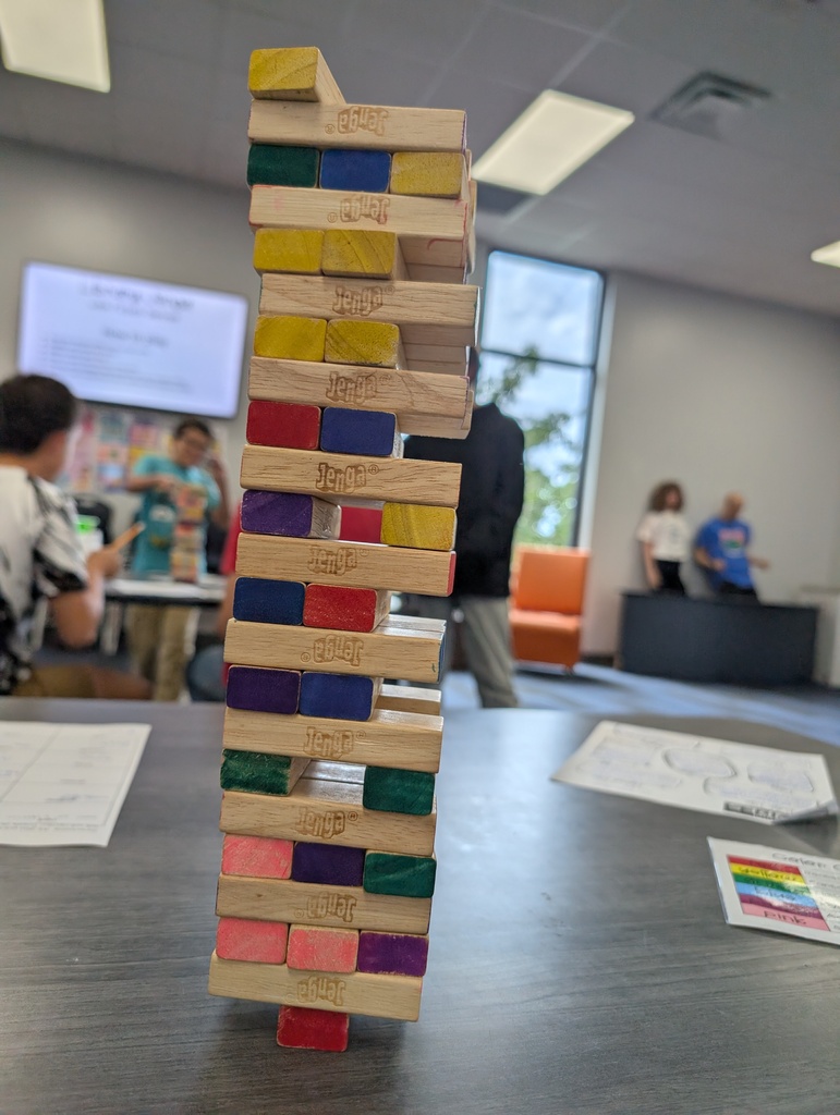 A stack of colorful wooden blocks on a table. People are walking in the background.