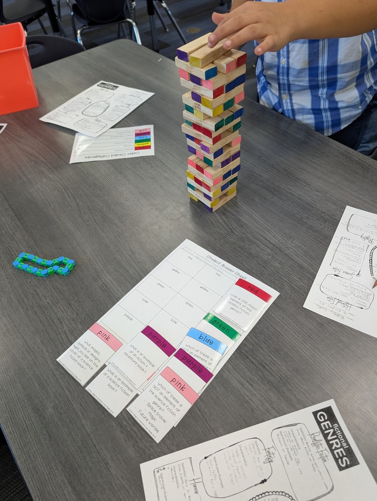 A person stacks wooden blocks in a tower on a table. Papers with writing and a rubber band are nearby.