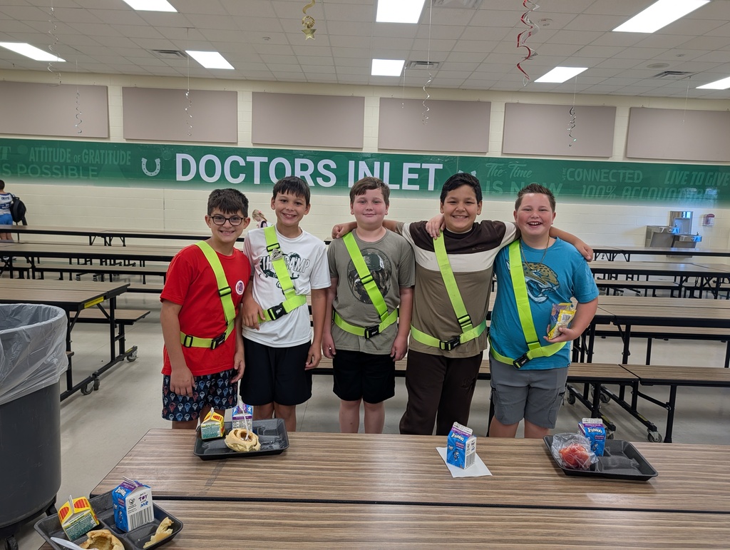 Five boys stand in a cafeteria, wearing safety harnesses. Trays with food are on a table in front of them.