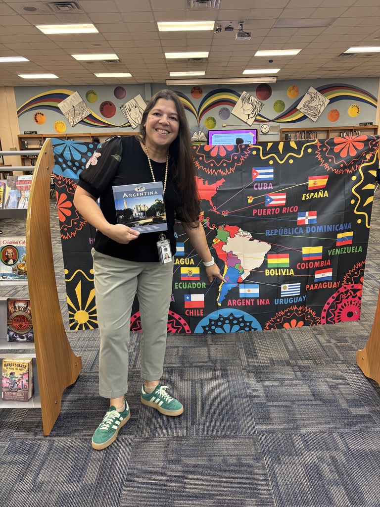 Woman holding a book stands before a colorful banner with flags from various countries.