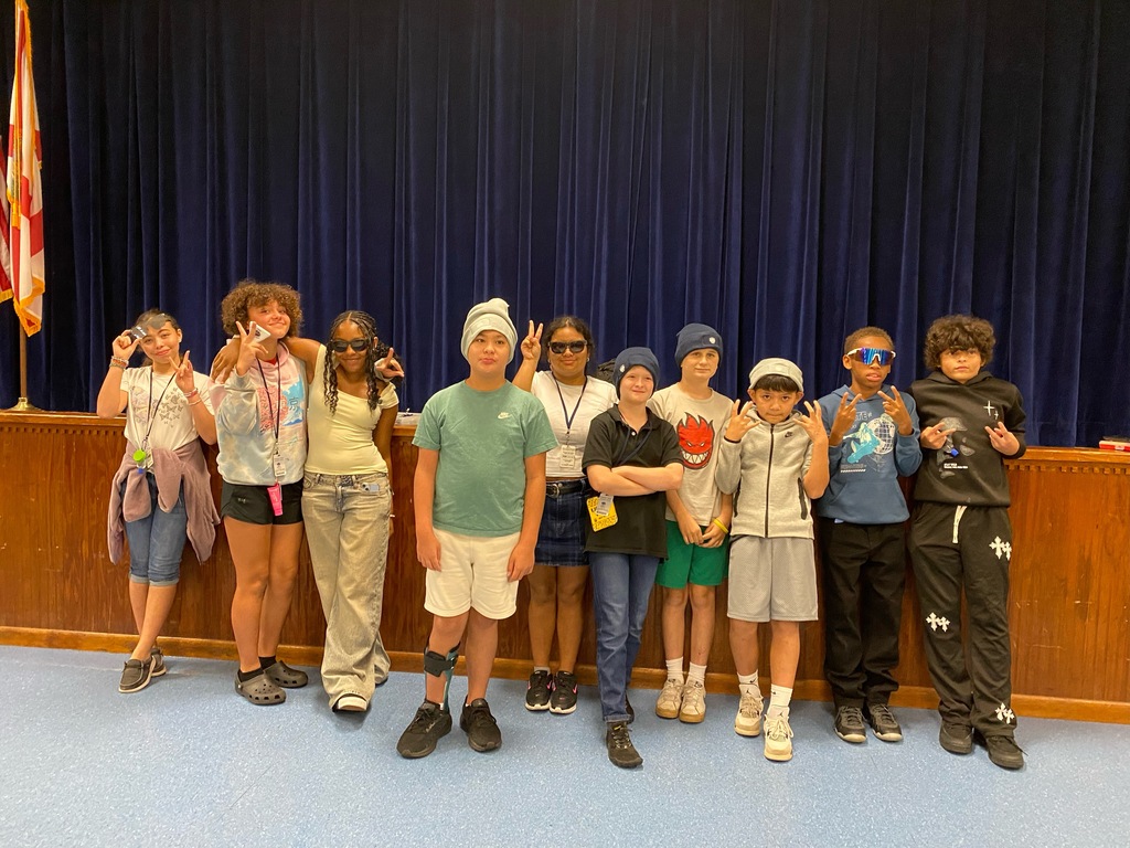 Eleven people, possibly students, stand in a line and pose for a photo in front of a stage.