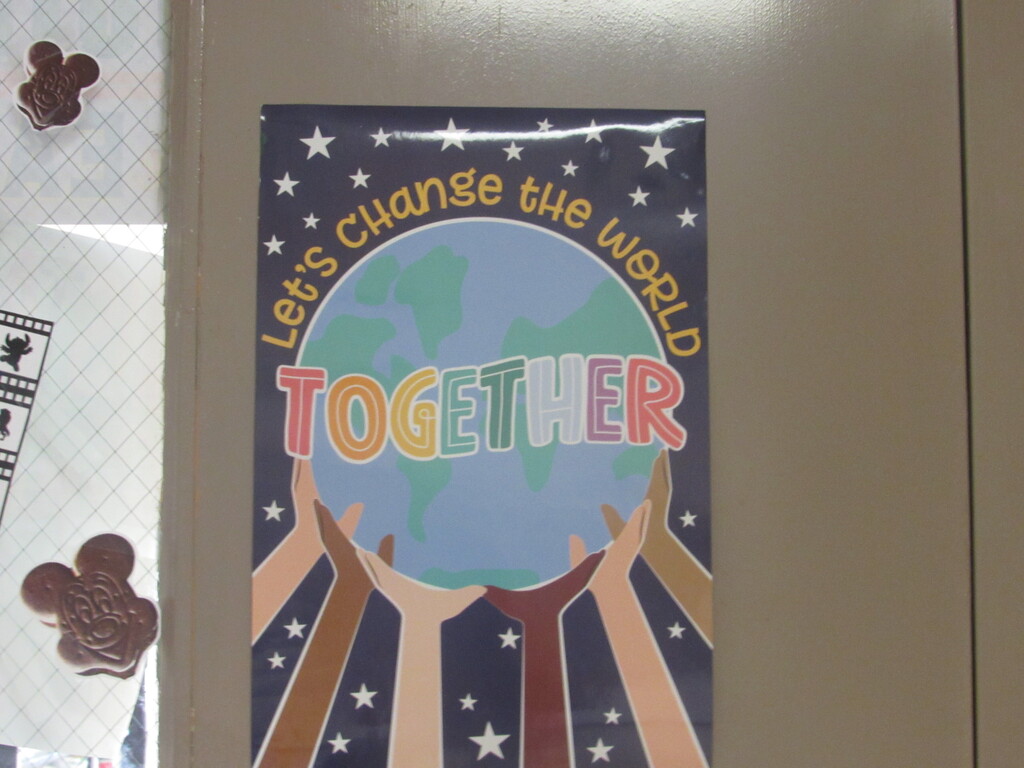 A poster with hands holding a globe reads "Let's Change the World Together." The background is a light brown, textured surface.