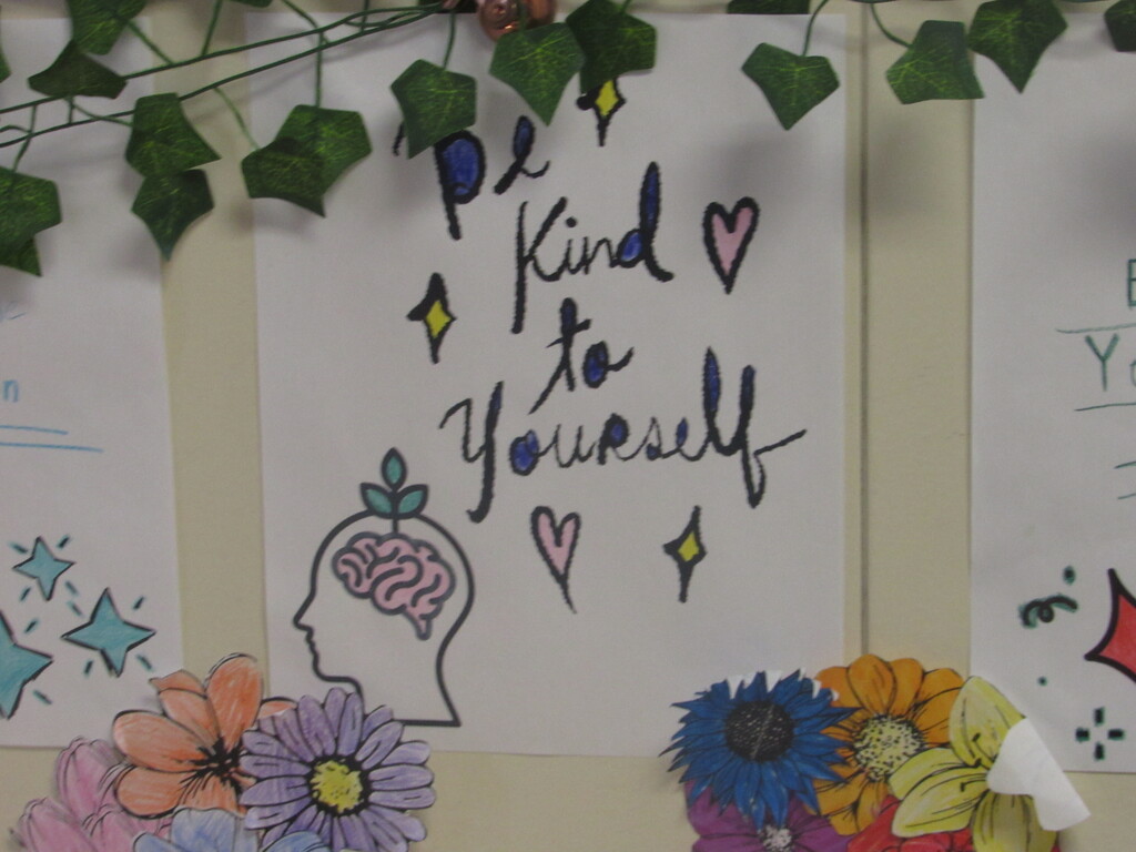 A white paper on a wall with drawings of flowers, a brain, and hearts. Text reads "Be kind to yourself."