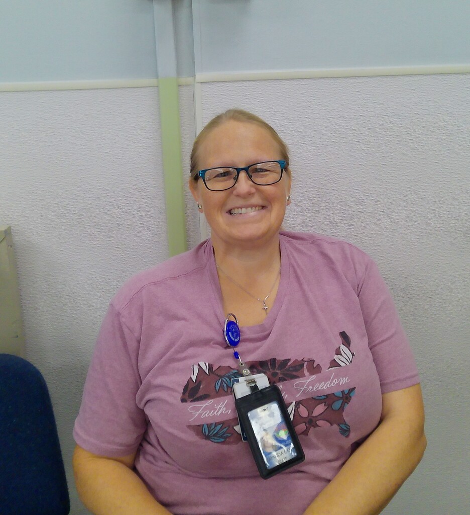 A smiling woman wearing glasses, a pink shirt, and a name tag with a photo ID.