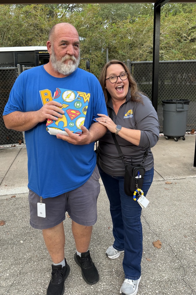 Mr. Jason in a blue shirt holding a gift bag with Mrs. Palmer in a grey pullover jacket.
