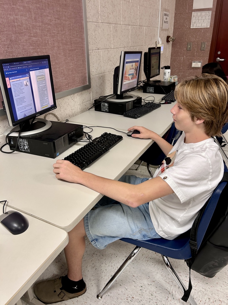 A boy using a computer in a classroom with three monitors, keyboards, and mice on a table.