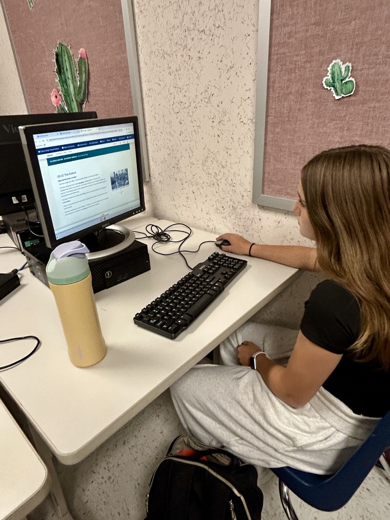 Person using a computer at a desk, with a thermos and a backpack on the floor.