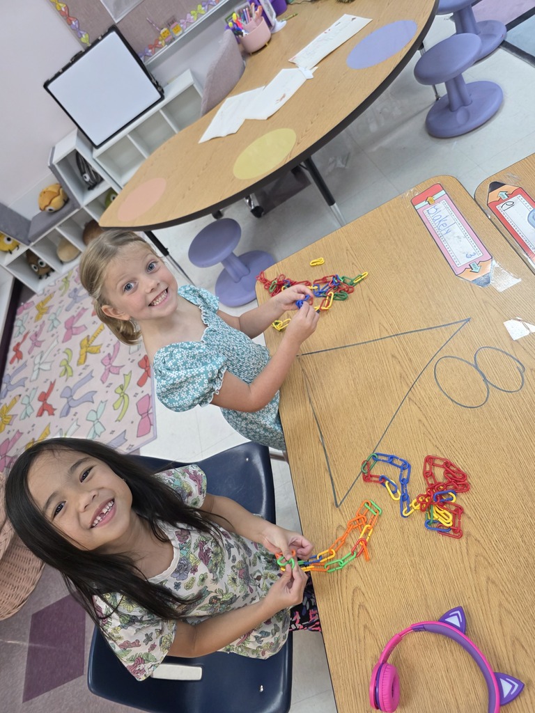 Two girls smiling, sitting at tables, using colorful craft materials and drawing on paper.