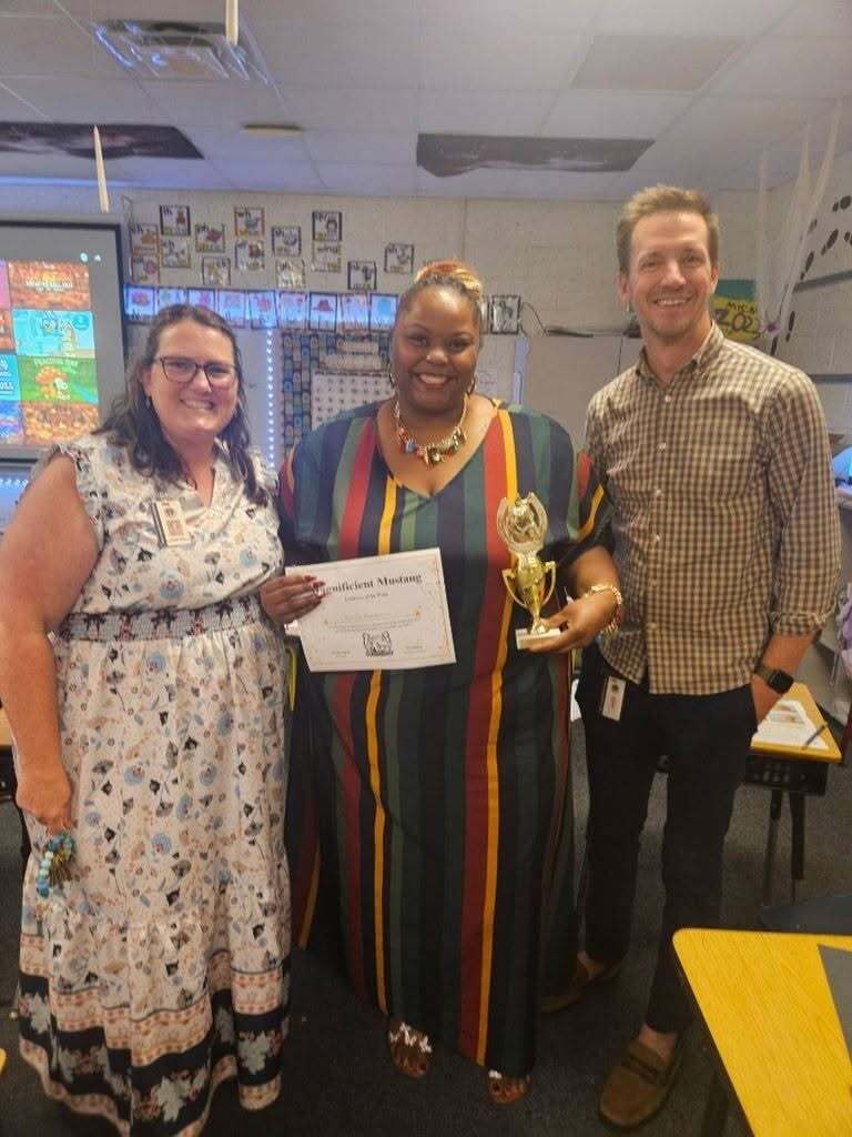 three people with the middle person holding a trophy and a certificate
