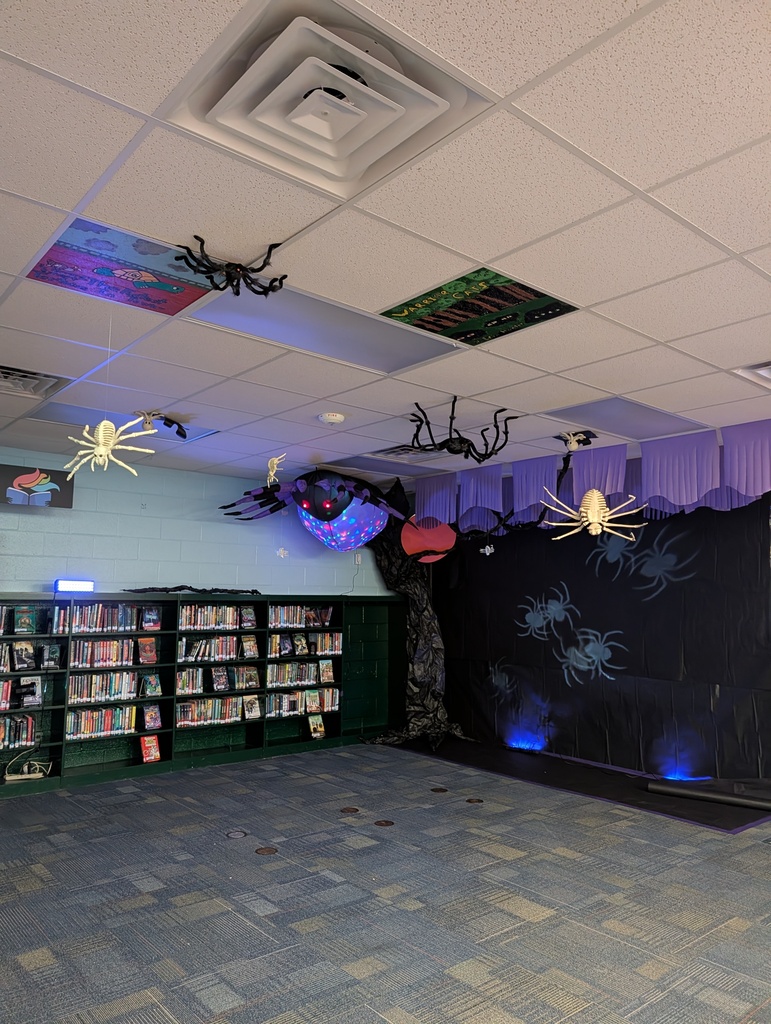 A room with bookshelves and a blue carpeted floor. The ceiling has Halloween decorations.