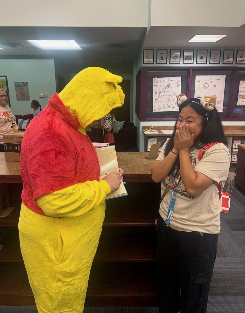 Two people in a library. Mr. Martin is dressed in a Winnie the Pooh costume. The other has a backpack and is covering mouth.