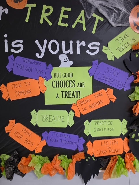 A Halloween-themed bulletin board with a black background. It features colorful candy-shaped messages, a ghost, and a pumpkin.