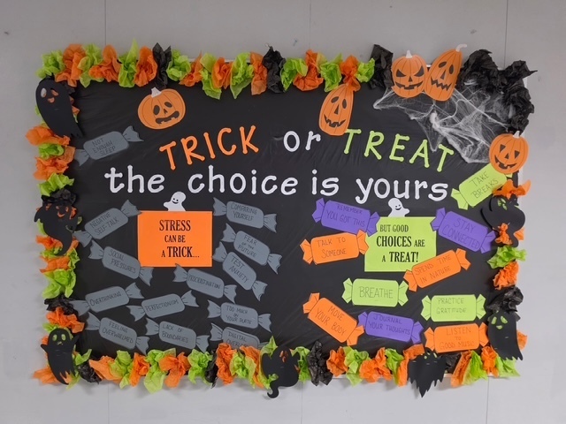 A bulletin board with Halloween decorations. The board says "TRICK or TREAT, the choice is yours". Various candies are attached to the board.