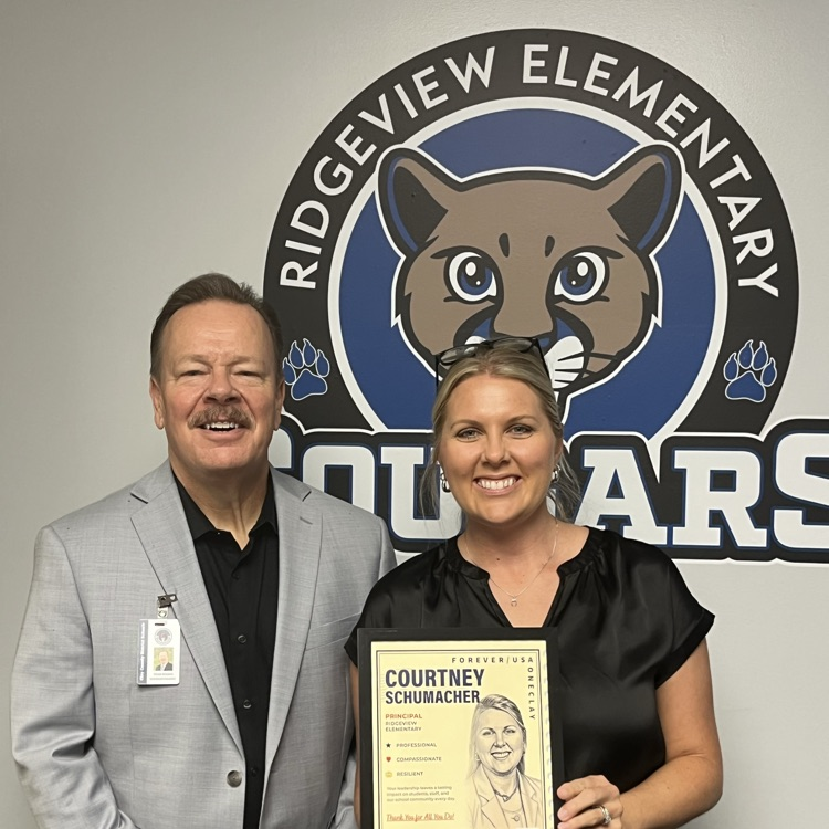 Superintendent stands with the principal in front of a cougars sign 