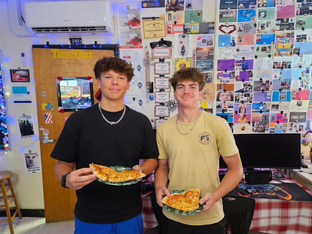 Two students standing with pizza.