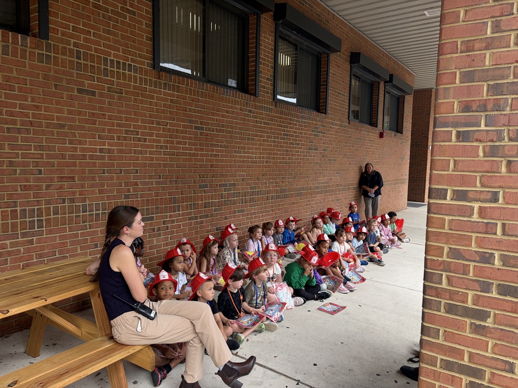 Students wearing red fireman hats and listening to firefighters