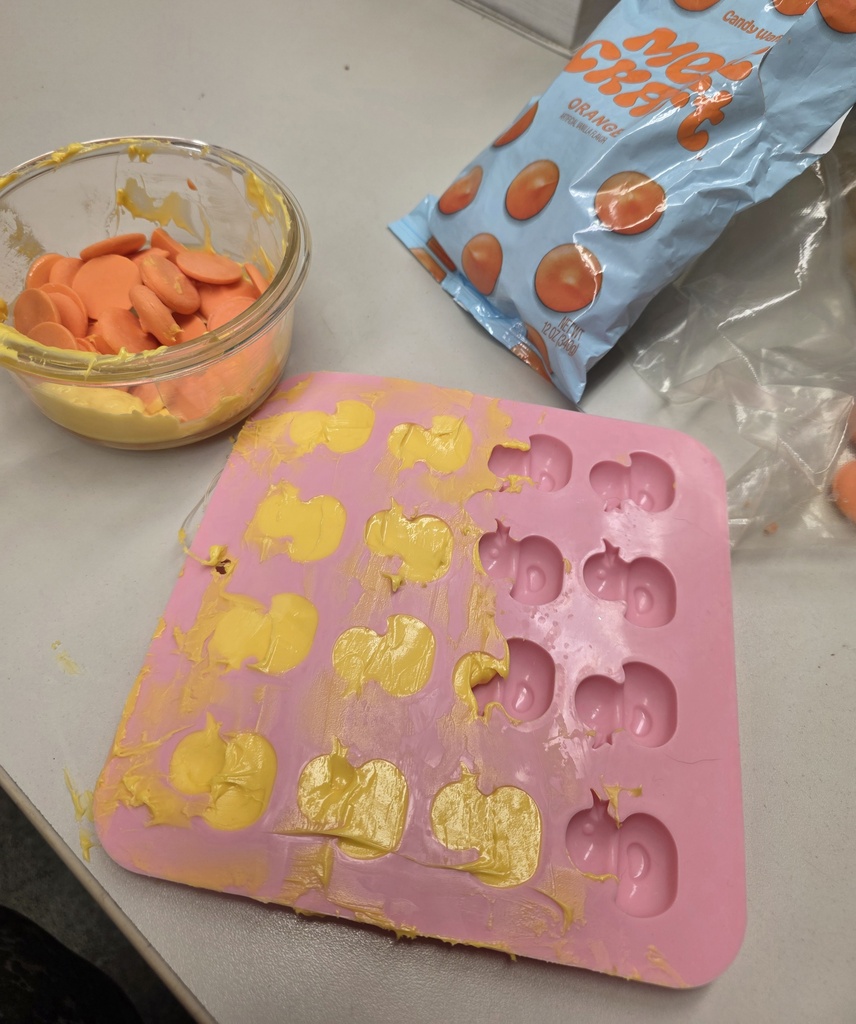 A pink plastic mold with yellow and orange decorations, a bowl of orange and yellow candy pieces, and a bag of snacks on a table.