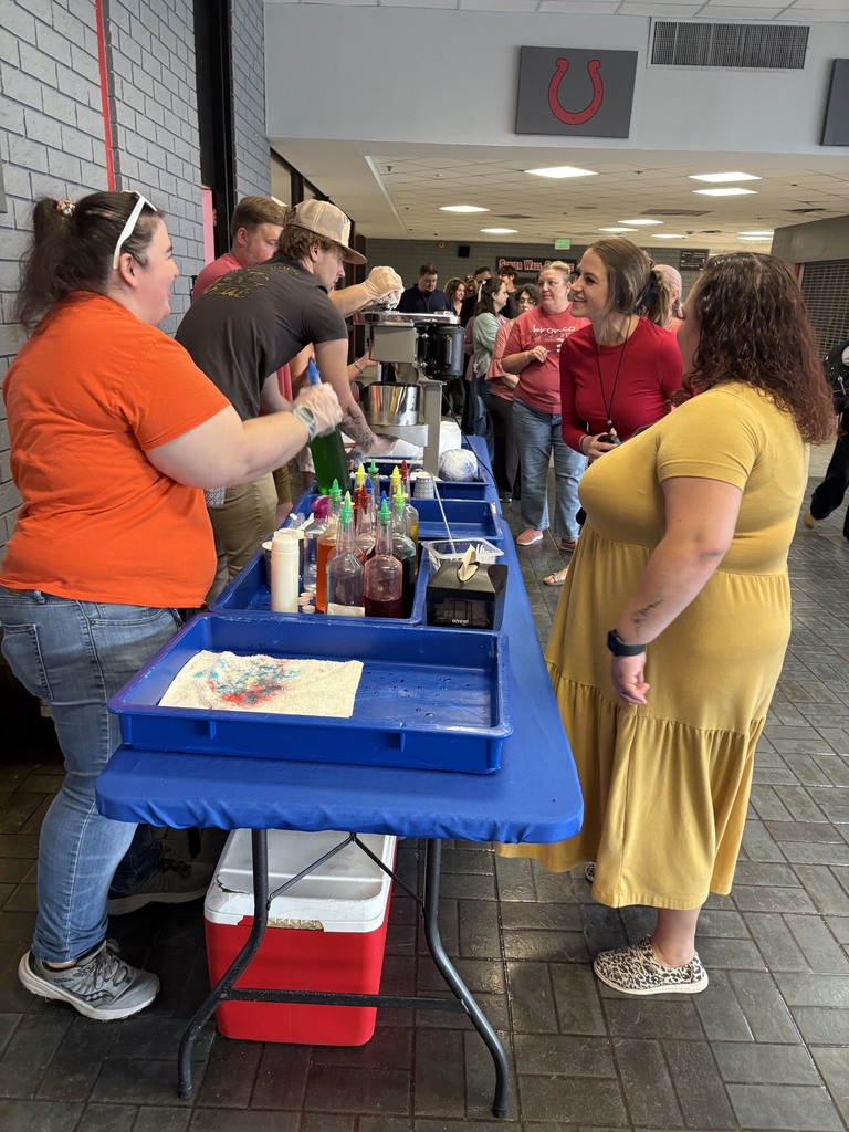 A table with a blue cover displays condiments and food. People stand behind it. One wears a yellow dress.