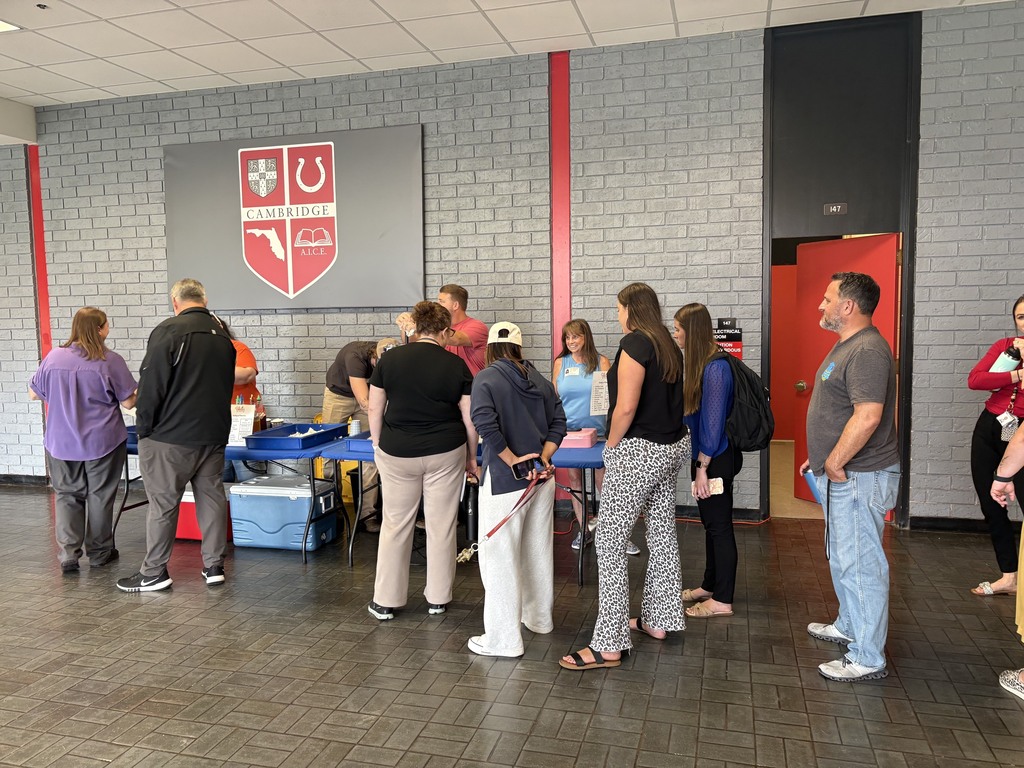 Indoor area with several people standing, some wearing backpacks, in front of a table with blue cover.