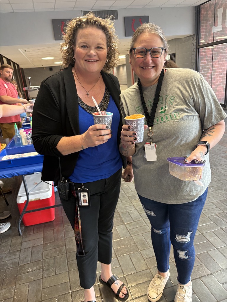 Two women smiling and posing for a photo. One has a cup and straw, the other has a bowl.